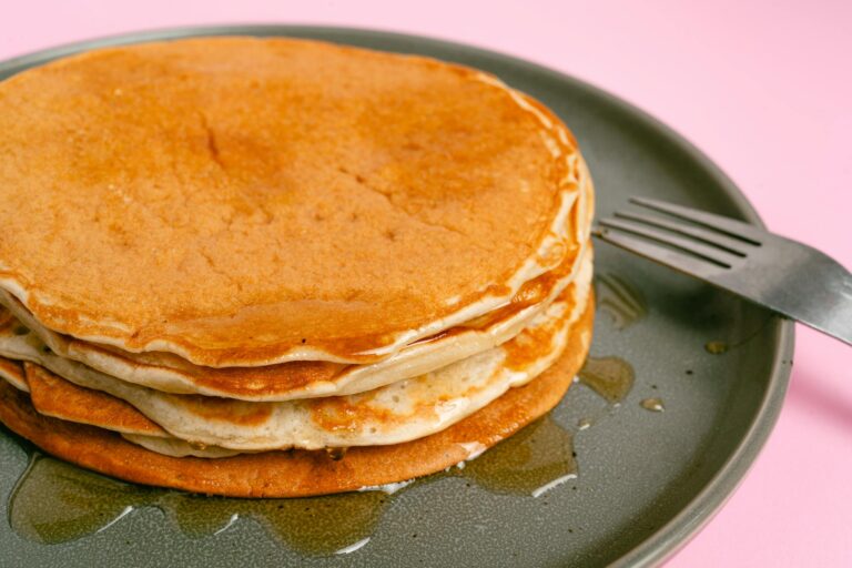 A tall stack of golden buttermilk pancakes with melting butter and maple syrup