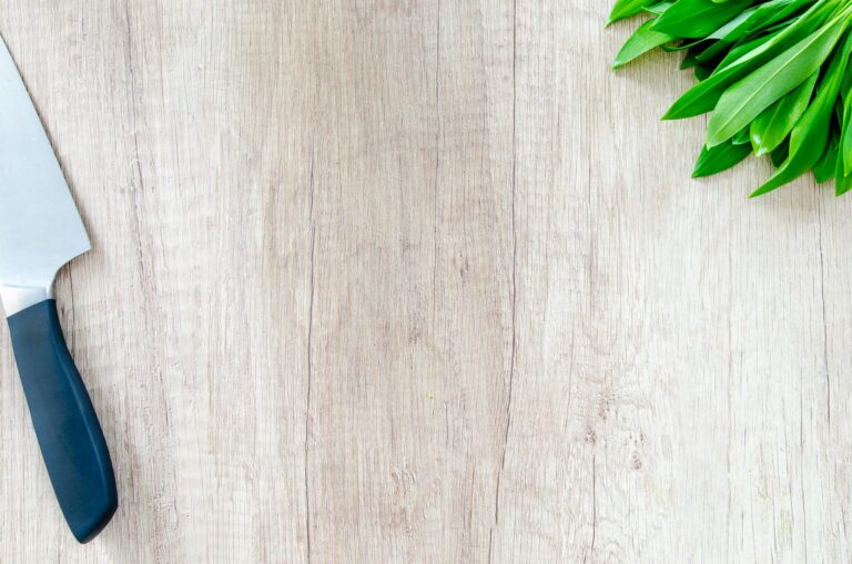Essential kitchen tools arranged on a wooden cutting board including a chef's knife and wooden spoons